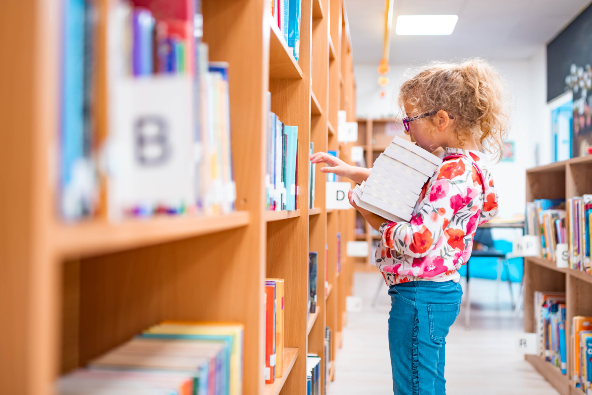 Young caucasian girl carrying a stack of books in a library.