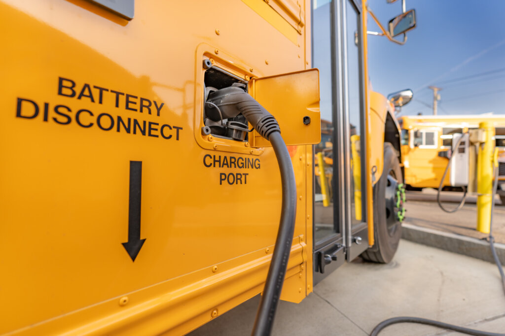 Image of a yellow electric school bus plugged in at a charging station.