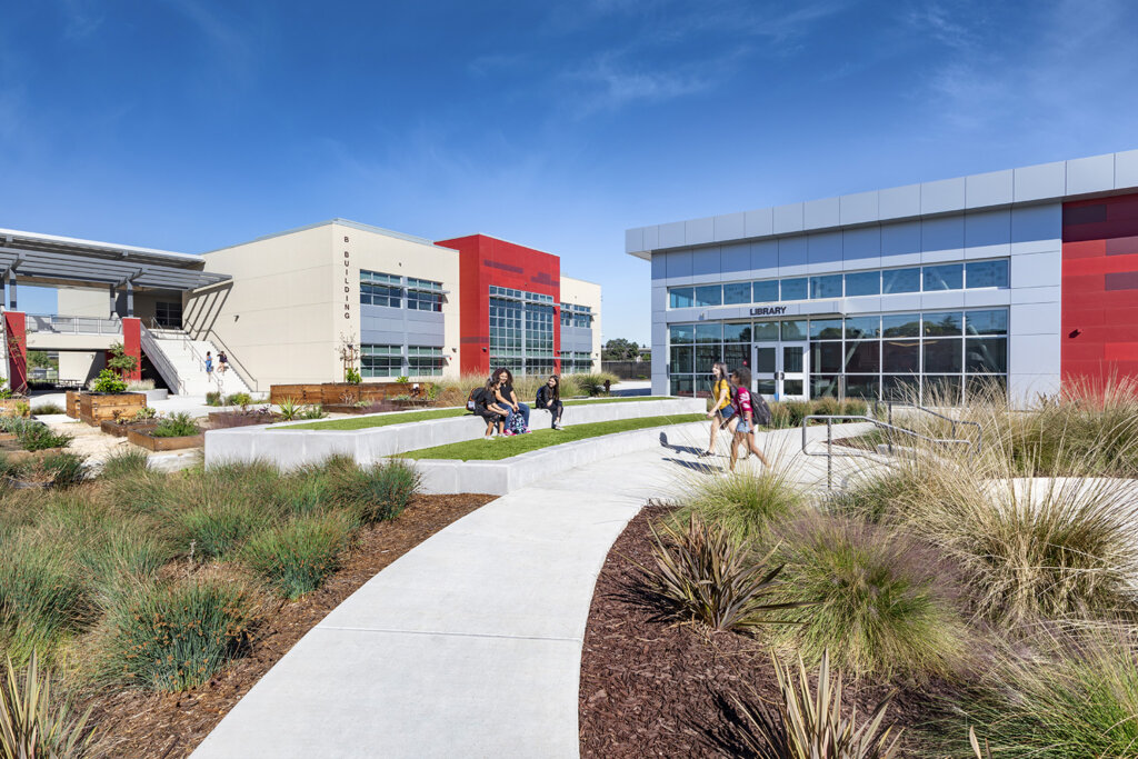 Image of students using outdoor green space adjacent to a modern, colorful school building.